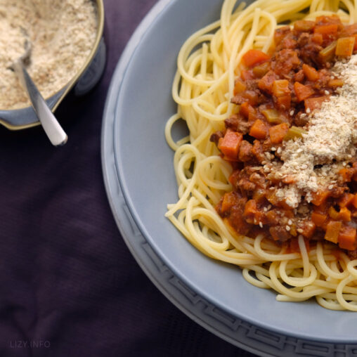 A dish with plantbased spaghetti topped with vegan grated parmesan cheese.