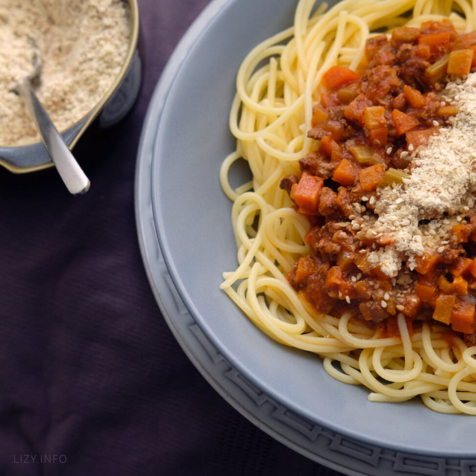 A dish with plantbased spaghetti topped with vegan grated parmesan cheese.